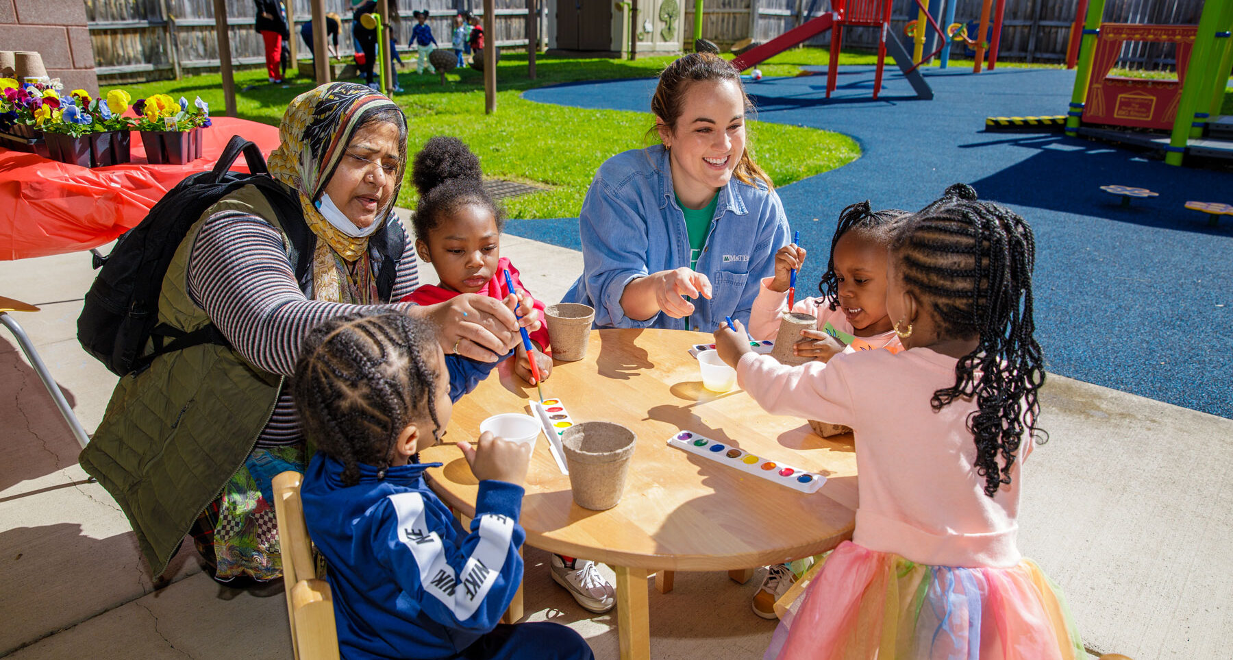 Adults help children paint flower pots outside