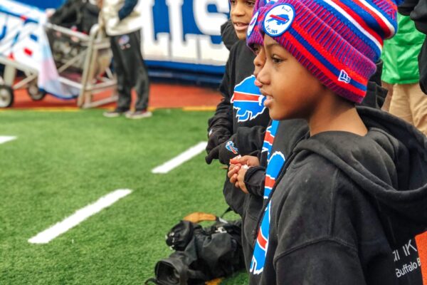 Young students in Bills gear watching flag football on the sidelines at New Era Field